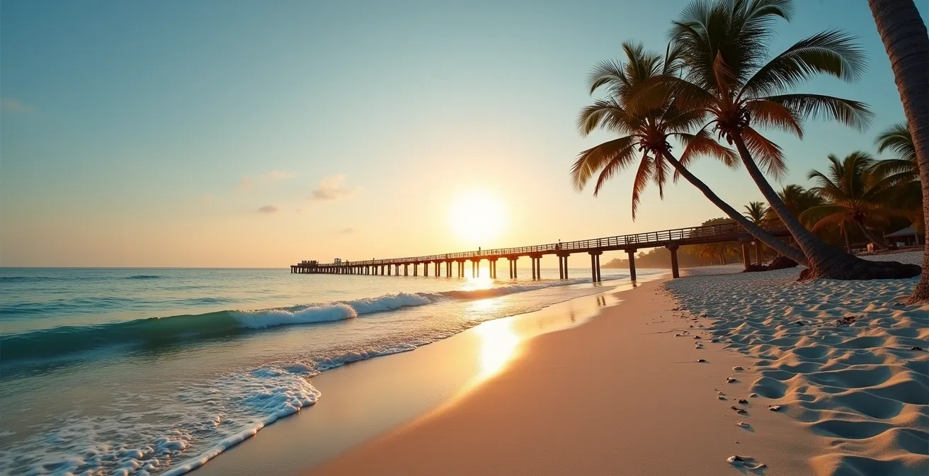 Playa Juanillo al amanecer con palmeras inclinadas y muelle de madera sin personas